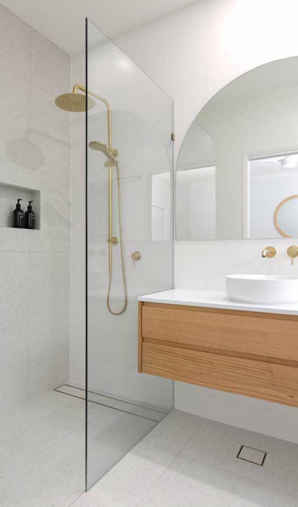 Modern bathroom with a glass-walled walk-in shower, brass fixtures, and a wooden floating vanity with a round vessel sink.
