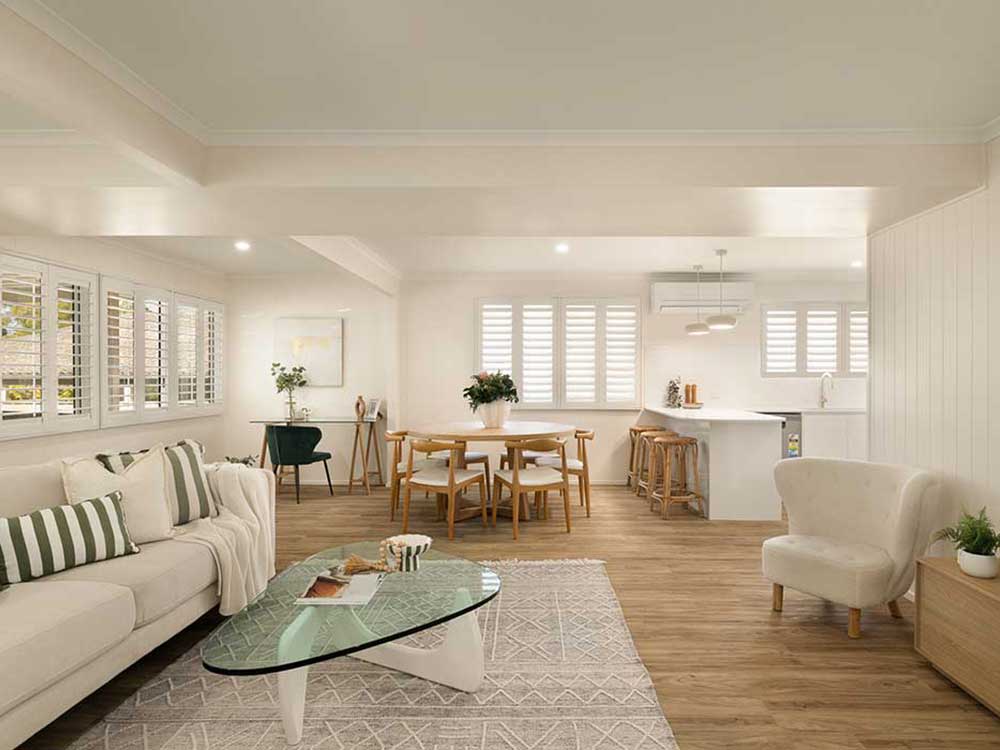 Bright open-plan living room and kitchen with white furniture, wooden floors, and large windows with shutters.